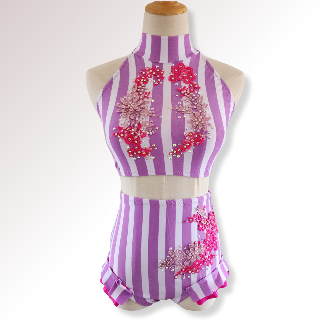 Purple and white striped leotard with pink floral embellishments on a mannequin against a white background.